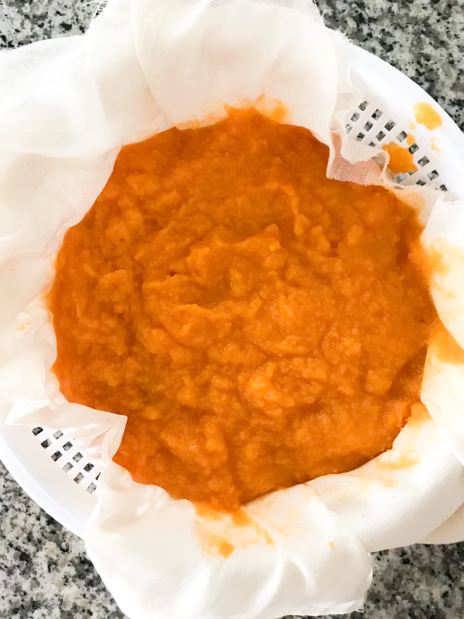 Overhead shot of bright orange homemade pumpkin puree draining in a cheesecloth-lined colander