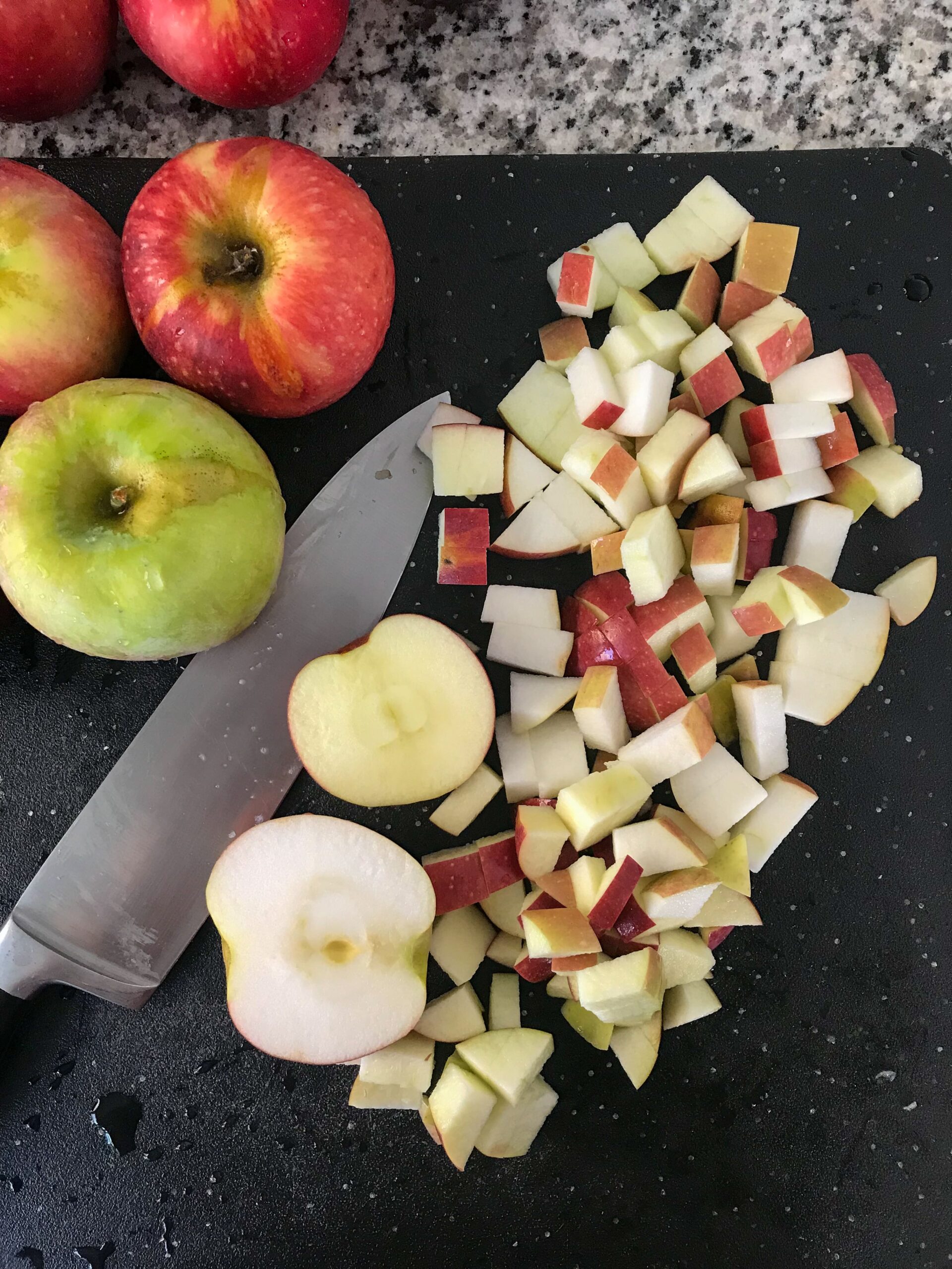 Overheard shot of chopped apples on a black cutting board with a chef's knife and whole apples off to the side