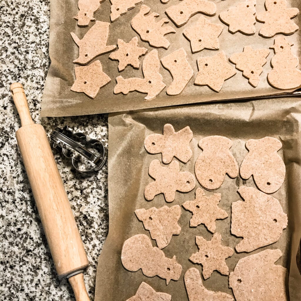 Rolled out salt dough ornaments arranged on two cookie trays with a rolling pin to the side