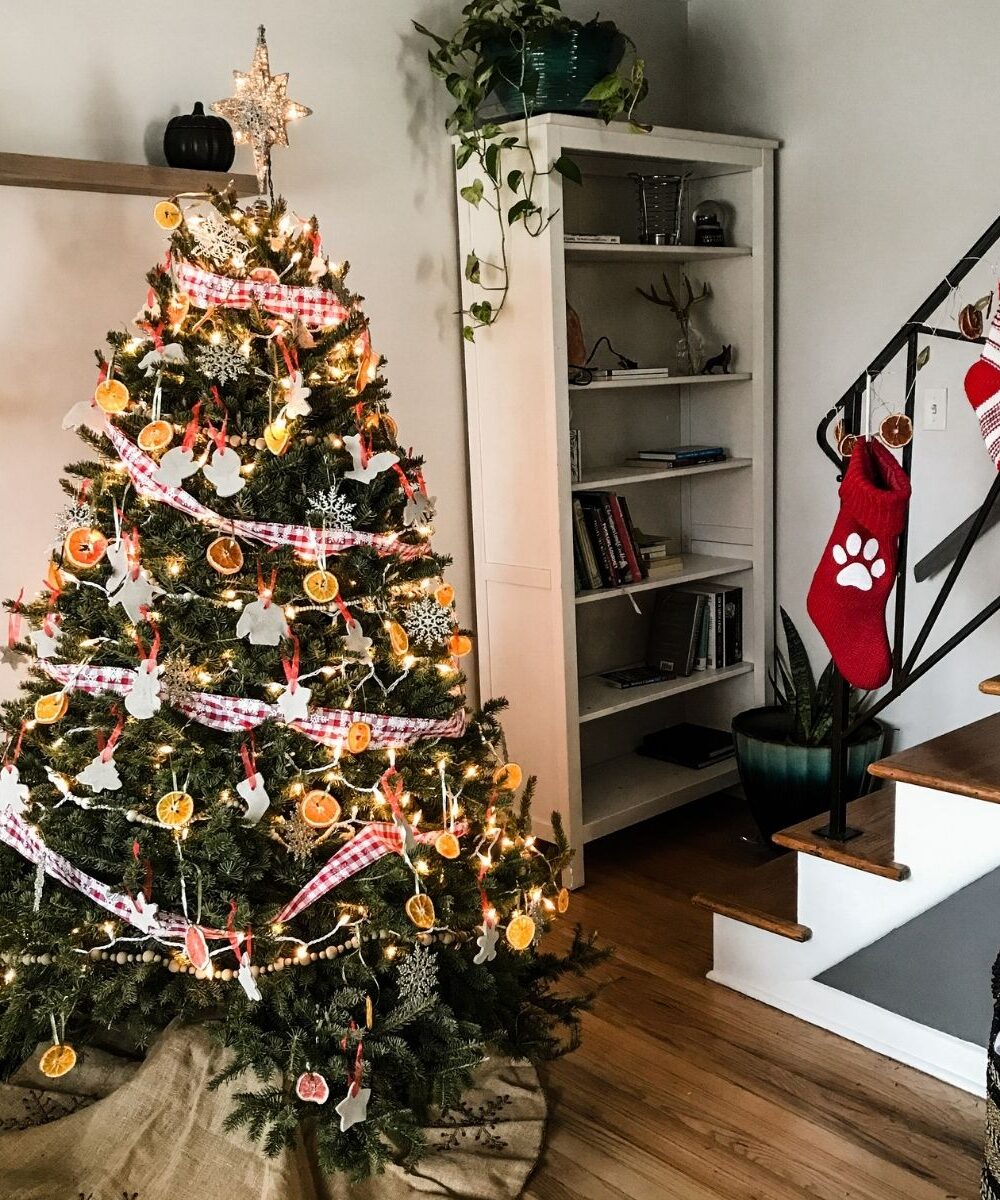 Image shows a decorated Christmas tree, featuring salt dough ornaments, in front of bookcase and next to a staircase railing with Christmas stockings.