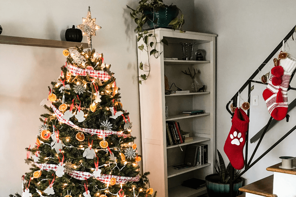 Image shows a decorated Christmas tree, featuring salt dough ornaments, in front of bookcase and next to a staircase railing with Christmas stockings.