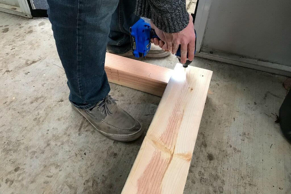 Image of a man's hands screwing a 2x6 board into a 4x4 post using an impact driver.
