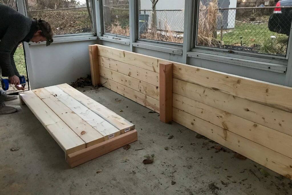 Image of a raised bed being built. One long side stands in the background while a man assembles another.