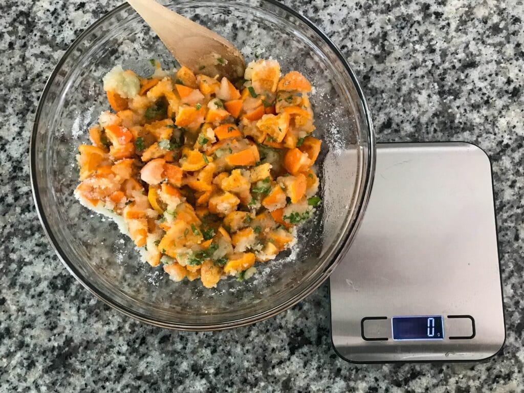 Image of a bowl of chopped oranges, sugar and herbs next to a kitchen scale