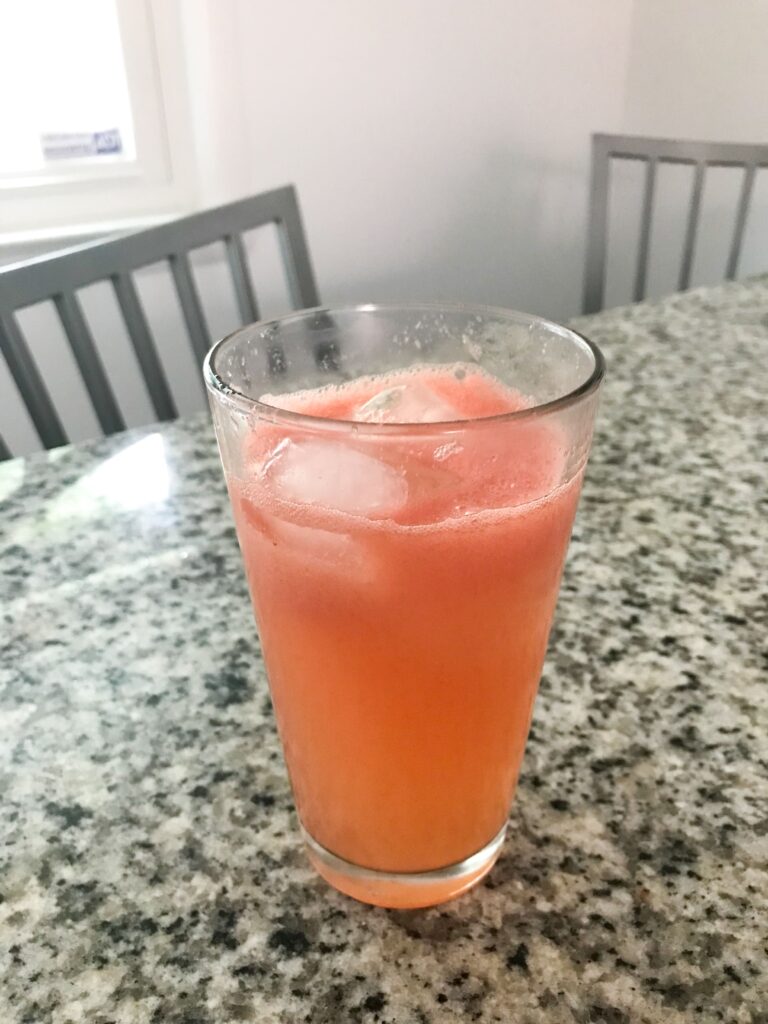 A very pink glass of Summer Watermelon and Herb Sour sitting on a granite countertop