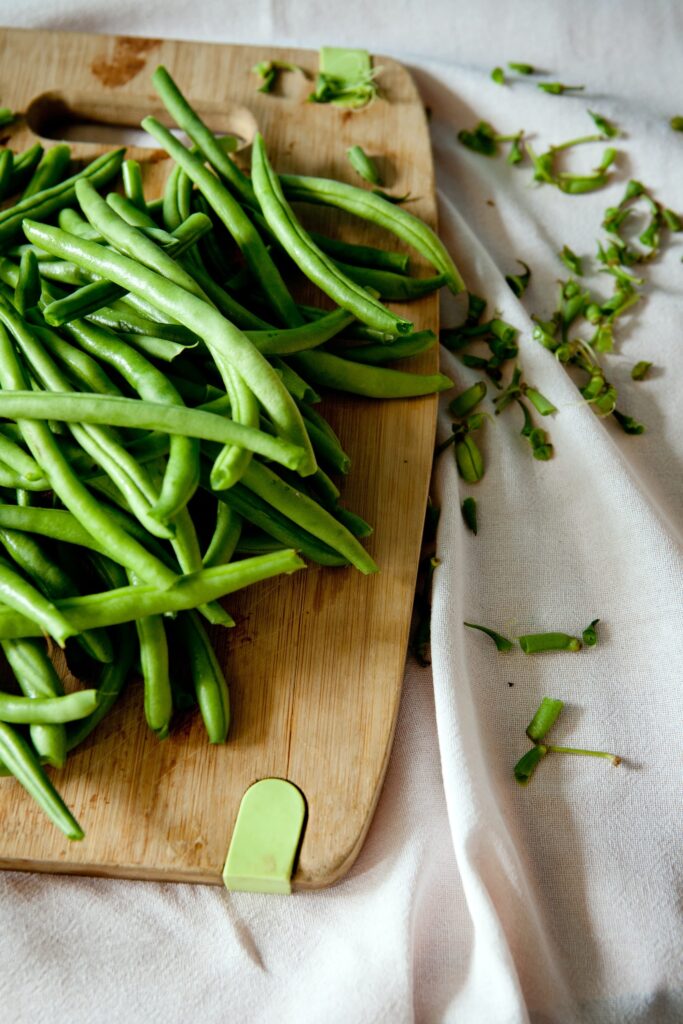 Image of a cutting board full of green beans, with the cut off ends to the side on a towel.