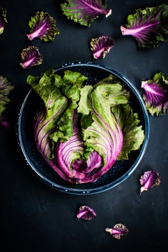 Image of a purple and green broccoli head in a bowl with leaves scattered around it