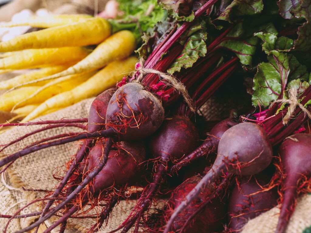 Image of a bundle of beets and a bundle of yellow carrots lying on burlap