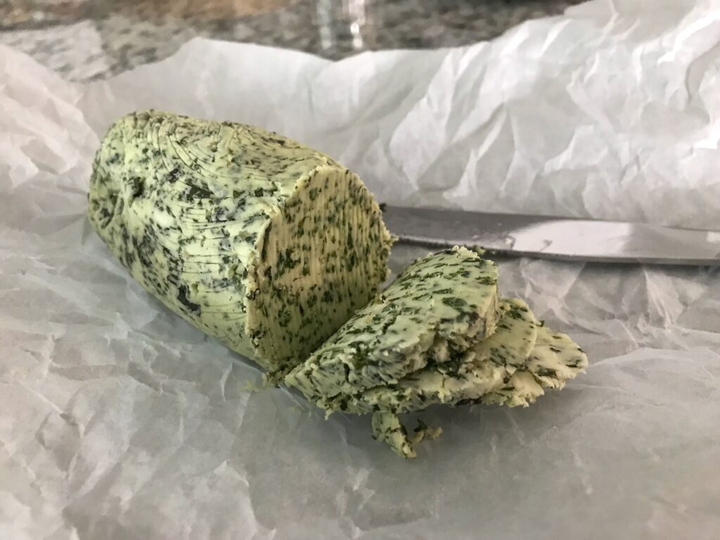 Log of basil garlic compound butter on parchment paper with a butter knife, granite countertop in the background; how to preserve fresh herbs