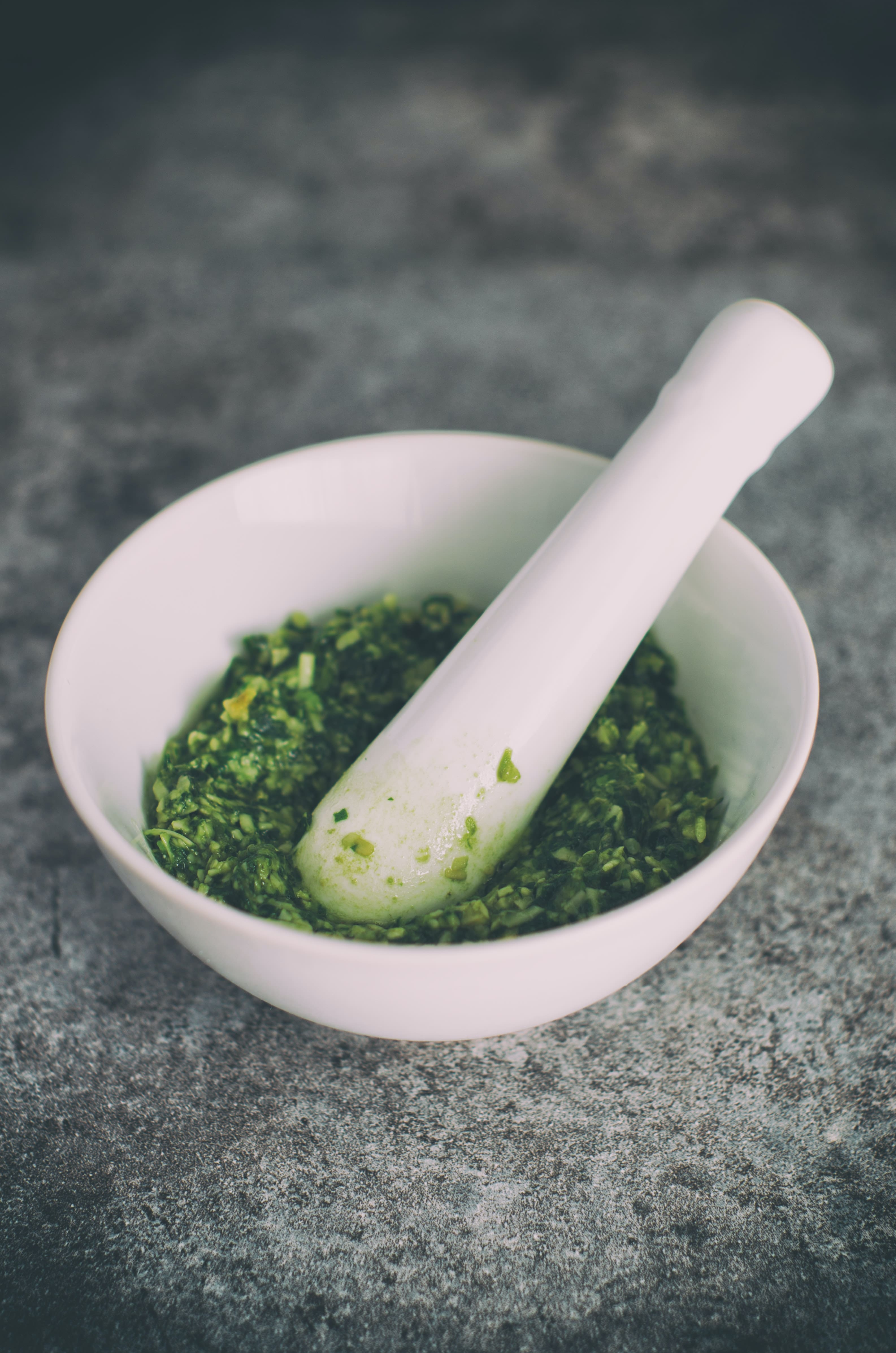White mortar and pestle full of bright green pesto on a dark countertop; how to preserve fresh herbs