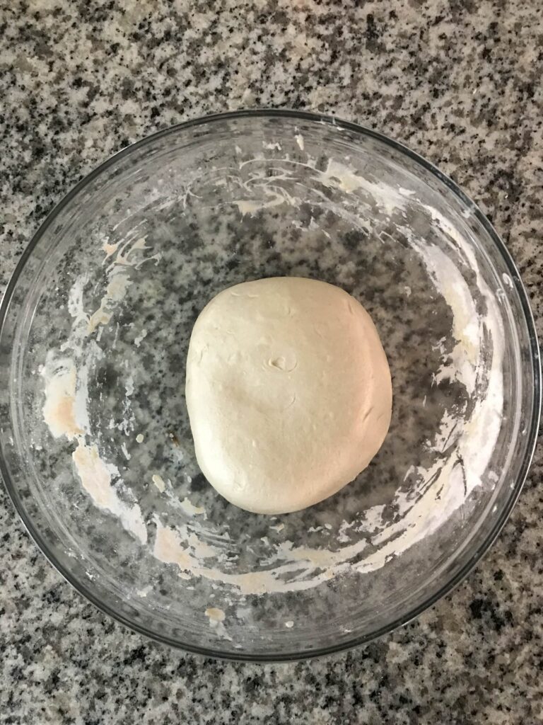 Glass bowl containing sourdough pizza crust dough at the beginning of bulk fermentation