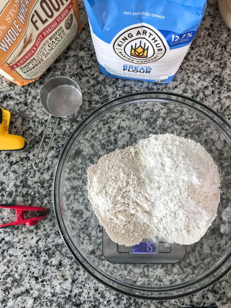 Glass bowl containing the bread flour and whole wheat flour for the autolyse. Bowl sits on a kitchen scale with the measurement 75g.