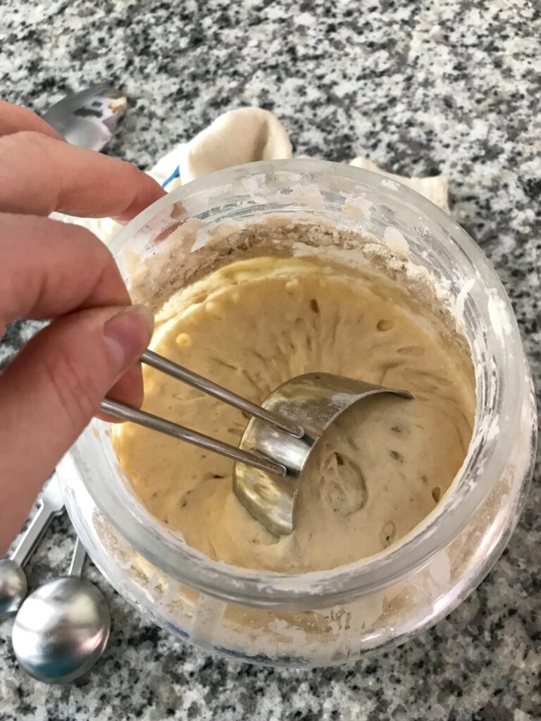 Overhead shot of a ripe sourdough starter being scooped out of the jar with a metal measuring cup