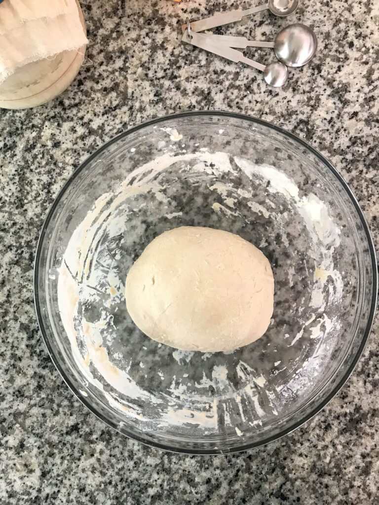 Overhead shot of a glass bowl containing the sourdough pizza crust dough after the final stretch and fold
