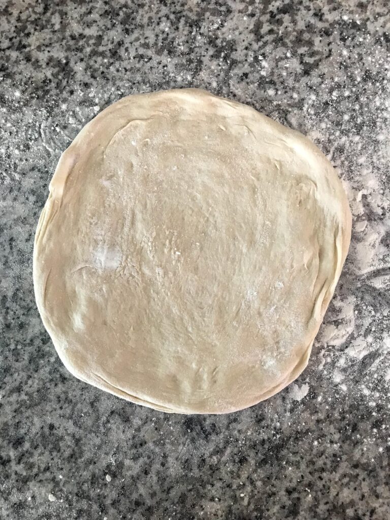 Stretched sourdough pizza crust resting on a floured countertop before going into the oven