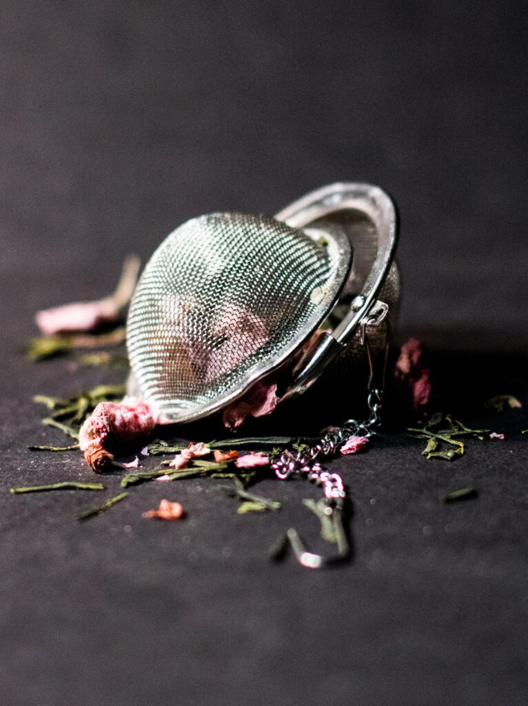 Herbal tea leaves spill out of a slightly open infuser ball on a gray background – herbal tea recipes