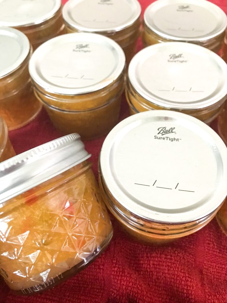 Many jars of peach pepper jam on a red dish towel. One is on its side
