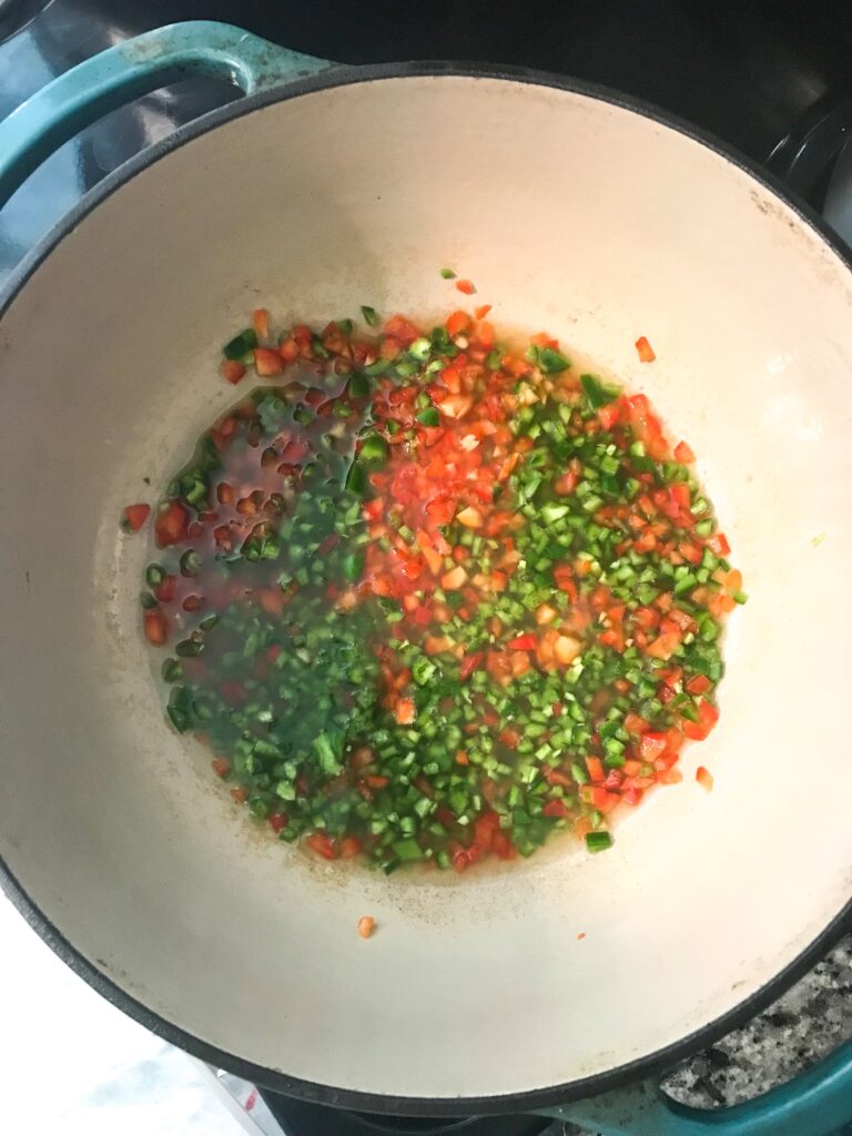 Overhead shot of a dutch oven containing finely chopped peppers simmering in apple cider vinegar – peach pepper jam