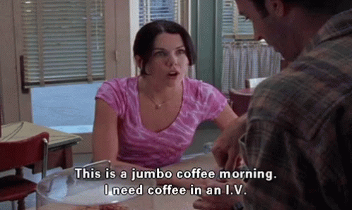 Gif of Lorelei in Gilmore Girls season 1 telling Luke, "This is a jumbo coffee morning. I need coffee in an IV." She sits at the diner counter wearing a pink tie dye t shirt.