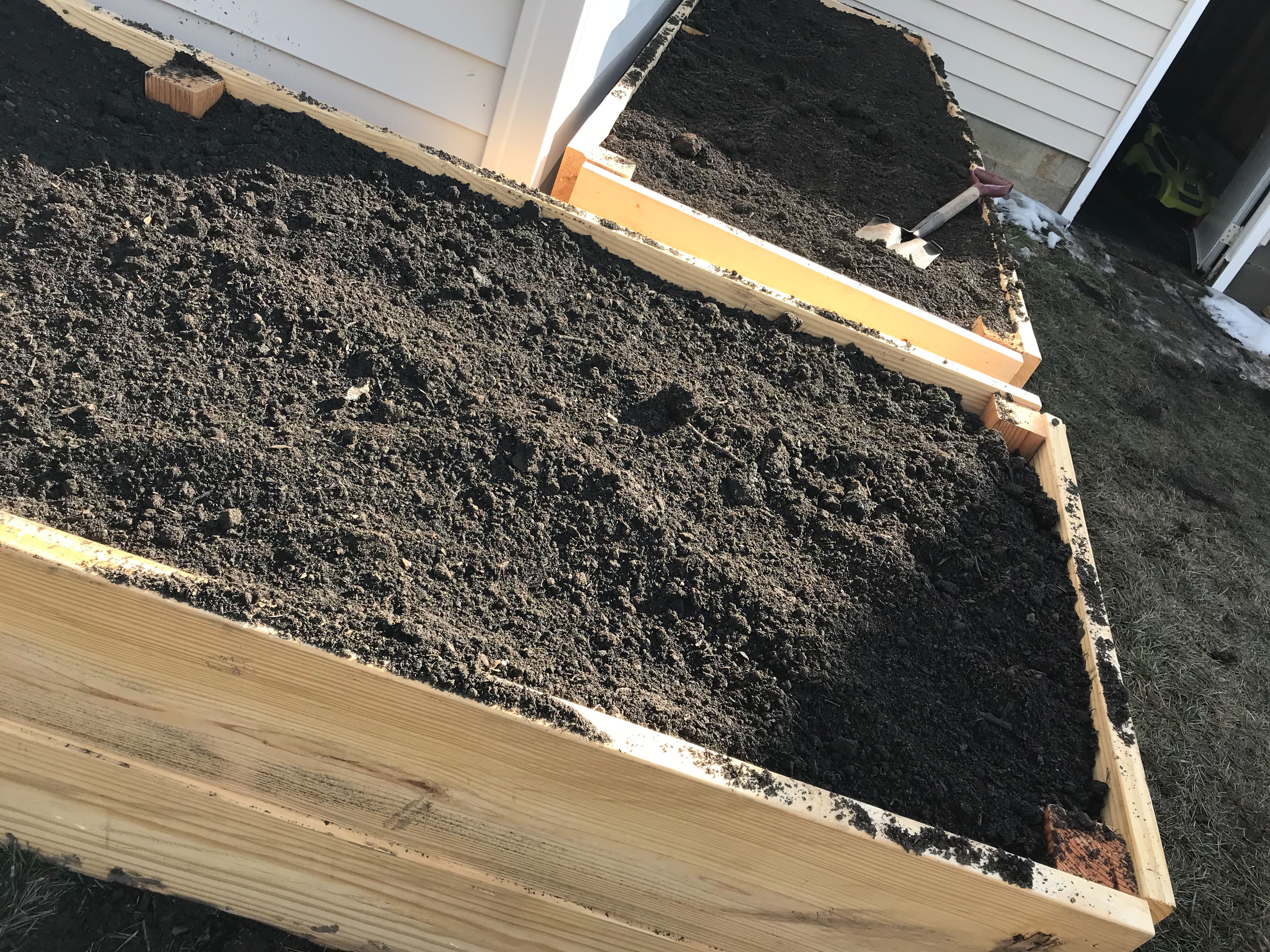 Close up of the corner of a wooden raised garden bed full of rich, black soil feed the soil
