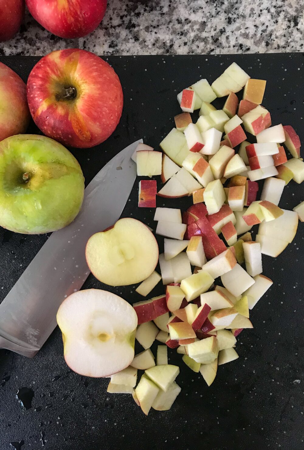 Overheard shot of chopped apples on a black cutting board with a chef's knife and whole apples off to the side