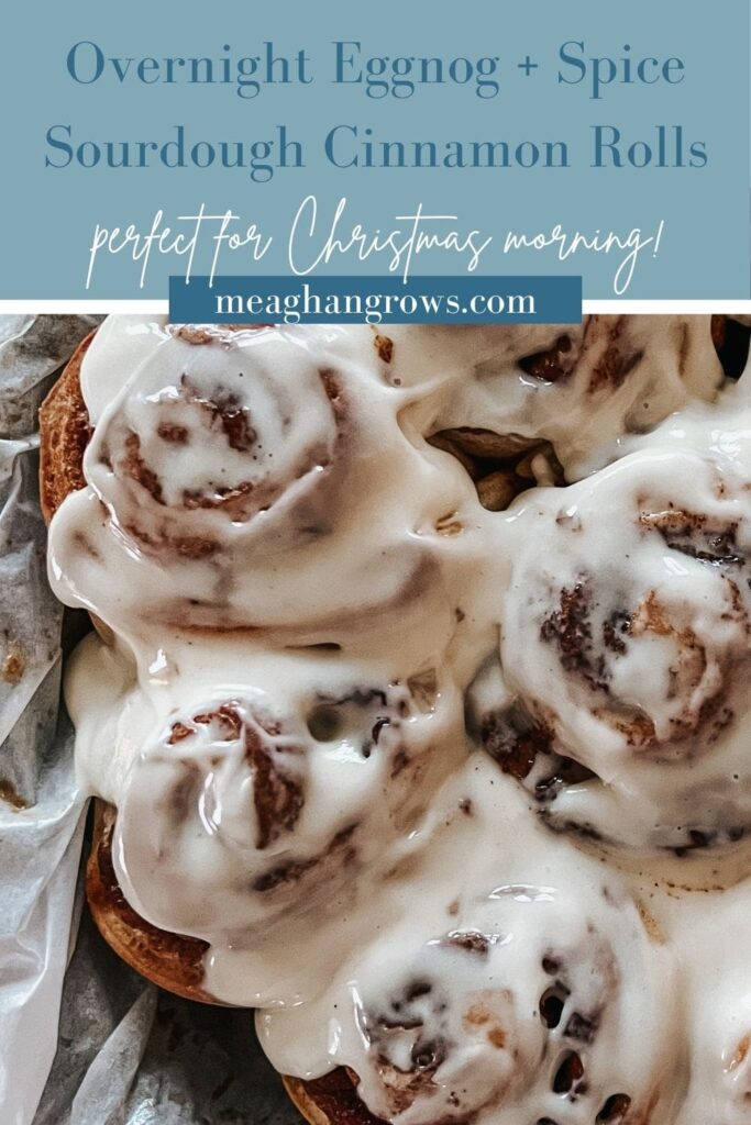 Pinterest pin containing a close up of iced sourdough cinnamon rolls and a blue banner reading, "Overnight eggnog + spice sourdough cinnamon rolls – perfect for Christmas morning!" and "meaghangrows.com"