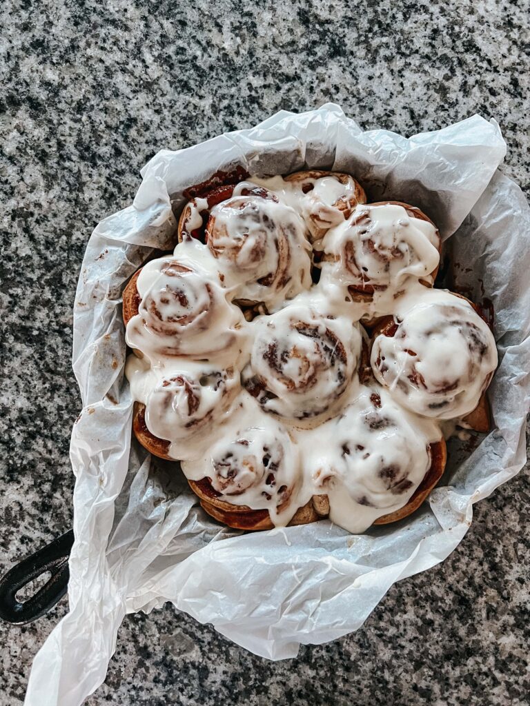Overhead shot of iced sourdough cinnamon rolls in a parchment-lined cast iron pan on a gray and white granite countertop