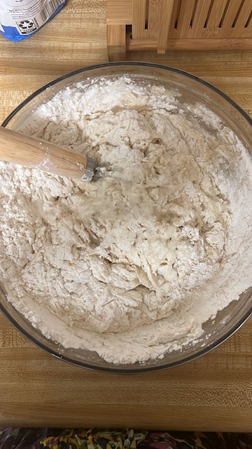 Overhead shot of a glass bowl with the ingredients for sourdough sandwich bread beginning to be combined with a Danish dough whisk. The ingredients are just beginning to reach the shaggy dough stage.